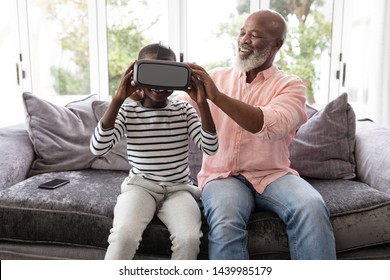 Front view of African american Grandfather helping his grandson to wear virtual reality headset in living room at home - Powered by Shutterstock