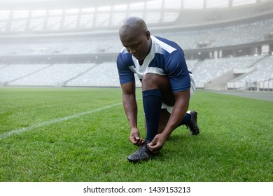 Front view of African american male rugby player tying shoelaces in the stadium - Powered by Shutterstock