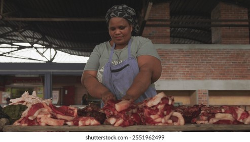 Front view of an African female butcher wearing a headscarf in a township workshop, selecting and picking fresh meat, slow motion - Powered by Shutterstock