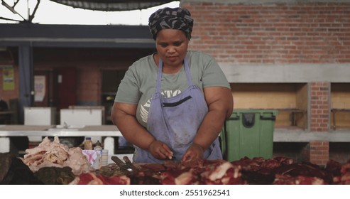 Front view of an African female butcher wearing a headscarf in a township workshop, cutting fresh meat with knife, slow motion - Powered by Shutterstock