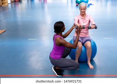 Front view of African-american Female trainer assisting disabled Caucasian senior woman to exercise with dumbbell in sports center. Sports Rehab Centre with physiotherapists and patients working - Powered by Shutterstock