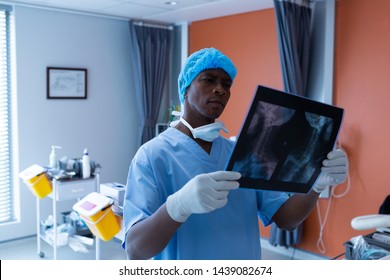 Front view of African-american male surgeon examining minutely x-ray in operating room of hospital. Healthcare workers in the Coronavirus Covid19 pandemic
