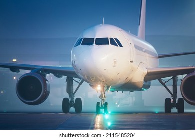 Front view of airplane at airport at foggy night. Plane during taxiing to runway for take off.
