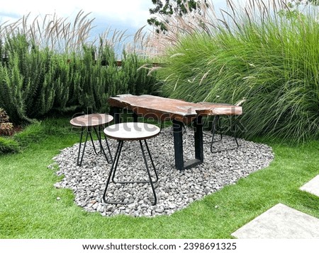Front view of arrangement of wooden tables and chairs standing on pebbles and green grass in park, forest, park in nature.