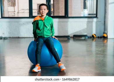 Front View Of Asian Boy Sitting On Fitness Ball In Gym