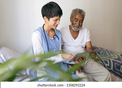 Front view of Asian female doctor and senior African-american male patient using digital tablet at retirement home