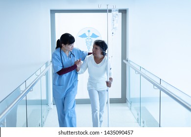 Front view of Asian female doctor helping mixed-race female patient to walk in the corridor at hospital - Powered by Shutterstock