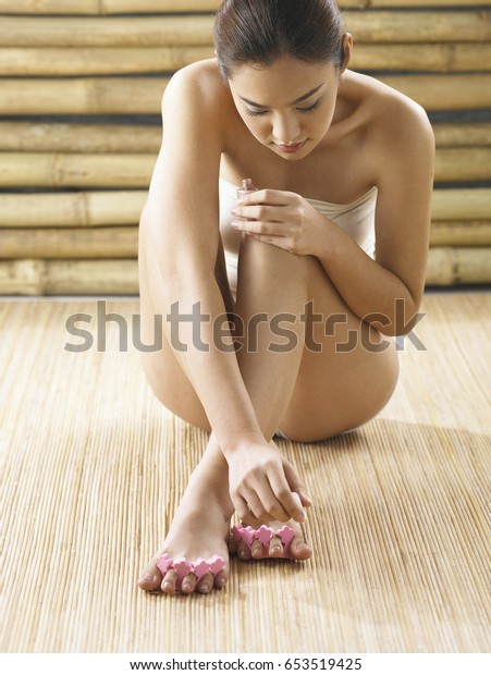 Front\
view of asian woman seated, painting her toe\
nails
