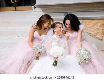 Front view of attractive bride in luxury wedding dress, which holding flowers, feeling happy and spending time with bridesmaids outdoor during wedding day