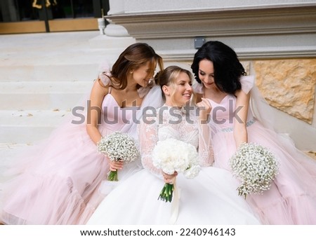 Front view of attractive bride in luxury wedding dress, which holding flowers, feeling happy and spending time with bridesmaids outdoor during wedding day