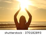 Front view of a back light of faithful woman silhouette holding sun on the beach at sunrise with a warm background