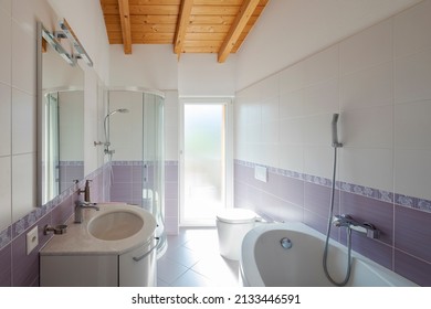 Front view bathroom with bathtub, shower, sink and toilet. Bright window. Exposed wooden beams. Nobody inside