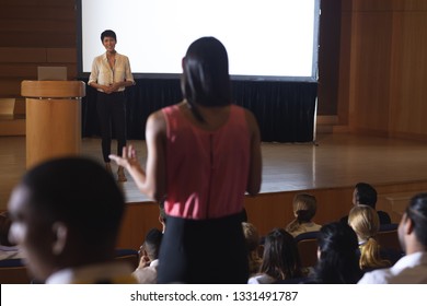 Front view of beautiful Asian businesswoman discussing while woman from the audience standing and asking query in the auditorium  - Powered by Shutterstock