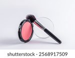 Front view of a beautiful open round pack of pink blush with a professional black makeup brush on it. white background. Product layout. A copy space