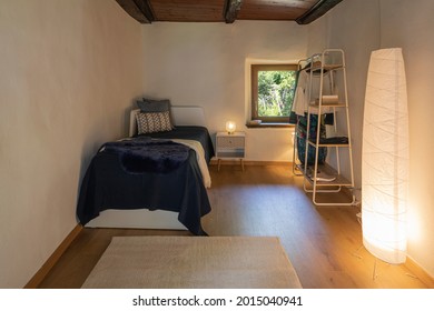 Front View Bedroom With Single Bed, Bedside Table With A Lamp Above And A Wardrobe On The Right. There Is A Small Window With A View Of Nature. Nobody Inside