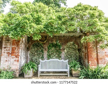 Front view of a bench surrounded by brick walls in the middle of a leafy garden, England
