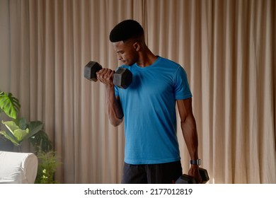 Front view of a Black African American young male exercising at home in his lounge lifting weights and dumbbells, bicep curls, keeping fit and healthy - Powered by Shutterstock