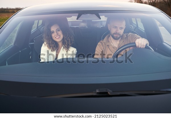 Front view in\
black car of focused male driver and smiling female passenger\
traveling by car out the\
town.