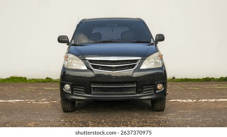 Front view of a black compact MPV parked outdoors on a gravel surface, reflecting natural light.