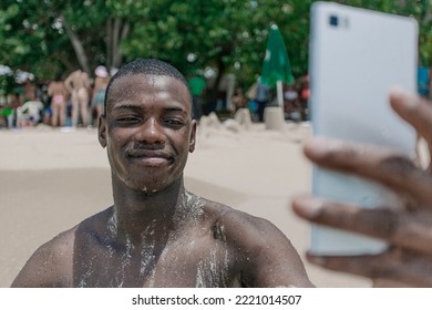 Front View Black Male Traveler Sitting On The Sand Near The Sea And Taking A Selfie During Summer Vacation At The Resort.