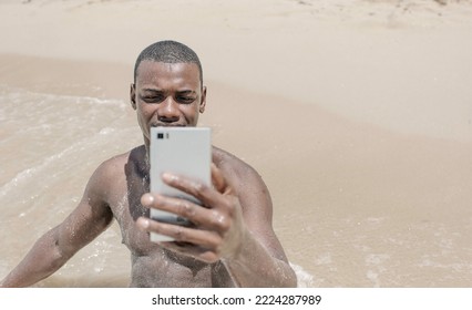 Front View Black Male Traveler Sitting On The Sand Near The Sea And Taking A Selfie During Summer Vacation At The Resort.