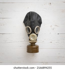 Front view of a black rubber gas mask on a white wooden background. Old army gas mask with filter