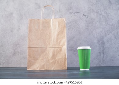 Front view of blank take away food bag and green coffee cup on wooden surface and concrete background. Mock up - Powered by Shutterstock