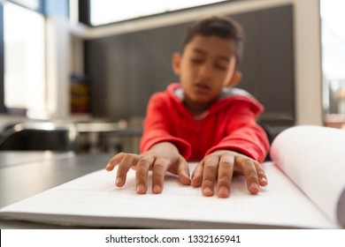 Front view of blind mixed-race schoolboy hands reading a braille book at desk in a classroom at elementary school