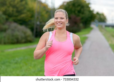 Front view of blonde smiling woman wearing sportswear running along river, close up.