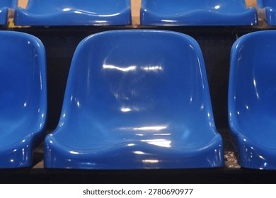 Front view of blue plastic stadium seats in neat rows, emphasizing symmetry, glossy texture, and empty seating arrangement in an indoor arena environment