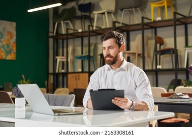 Front View Of Boy With Beard Sitting At Table, Designing. Handsome Designer Writing, Using Laptop, Looking At Screen. Concept Of Modern Urban Lifestyle, Shopping, Designing.