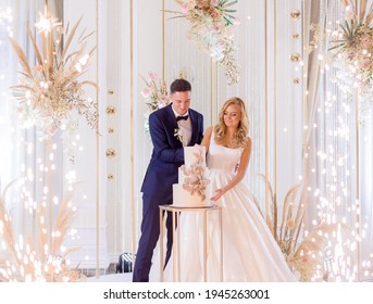 Front view of bride and groom, standing on bright stage with decoration, cutting wedding cake together
