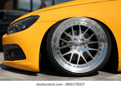 Front view of a bright yellow modified sports car showing low suspension, stylish multi-spoke alloy wheels, and modern headlight design on a paved road.