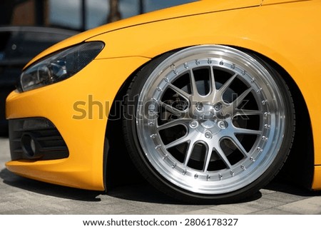 Front view of a bright yellow modified sports car showing low suspension, stylish multi-spoke alloy wheels, and modern headlight design on a paved road.