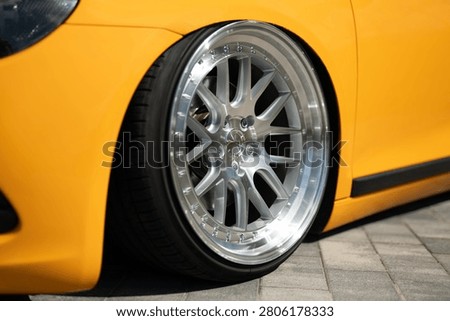 Front view of a bright yellow modified sports car showing low suspension, stylish multi-spoke alloy wheels, and modern headlight design on a paved road.