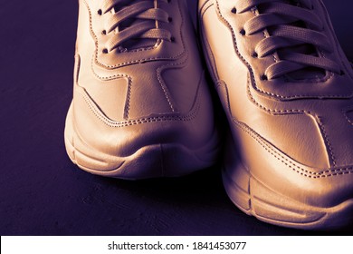 Front View Of Bronze Colored Chunky Sole Sneakers Over Dark Purple Background. New Unisex Tied Laces Shoes For Active Lifestyle, Fitness And Sports. Close-up. 