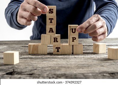 Front view of a businessman arranging wooden cubes in a structure reading Start up. Conceptual of business startup and strategy.