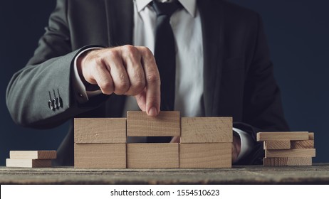 Front view of a businessman building a structure of wooden pegs in a conceptual image of business vision and start up. 