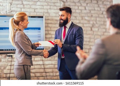 Front view of businessman receiving award from businesswoman in front of business professionals applauding at business seminar in office building