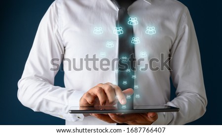 Front view of a businessman using digital tablet with many glowing people icons coming out of it. Conceptual of customer service and social media interactions.