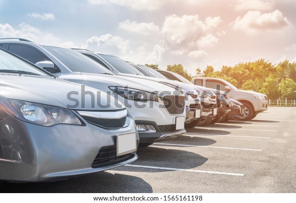 Front view car parking in asphalt parking lot in\
a row with white cloud and blue sky background. Outdoor parking lot\
with fresh ozone and green environment of travel transportation\
technology concept