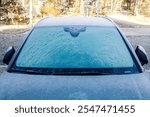 Front view of a car windshield covered with ice and frost on a winter day.