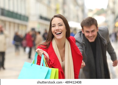 Front View Of A Casual Couple Of Shoppers Running In The Street Towards Camera Holding Colorful Shopping Bags