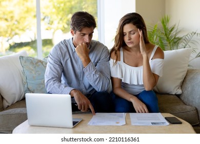 Front View Of A Caucasian Couple At Home, Sitting In The Living Room On A Couch Looking At Paperwork And Using A Laptop Computer