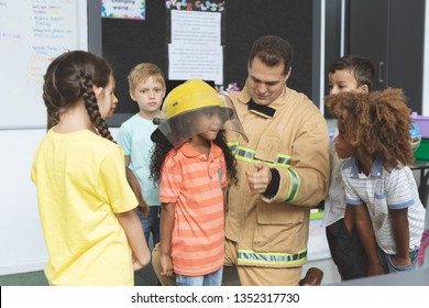 Front View Of A Caucasian Firefighter Interacting With School Kids While One Of Them Holding Fire Helmet On Her Head With Classmates Arround Her 