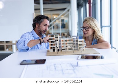 Front view of Caucasian male and female architect discussing over architectural model at table in a modern office. This is a casual creative start-up business office for a diverse team - Powered by Shutterstock