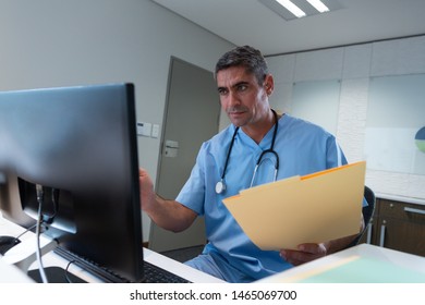 Front View Of Caucasian Male Surgeon Working On Computer At Desk In Hospital. Healthcare Workers In The Coronavirus Covid19 Pandemic