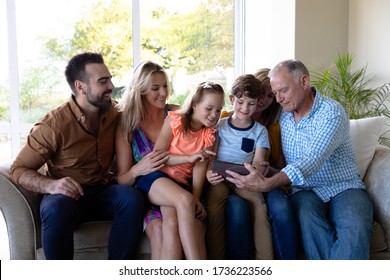 Front View Of A Caucasian Multi-generation Family In The Living Room At Home, Sitting On A Couch Together Looking At A Tablet Computer