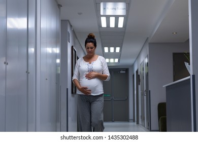 Front view of Caucasian pregnant woman touching her belly while walking in the corridor at hospital - Powered by Shutterstock