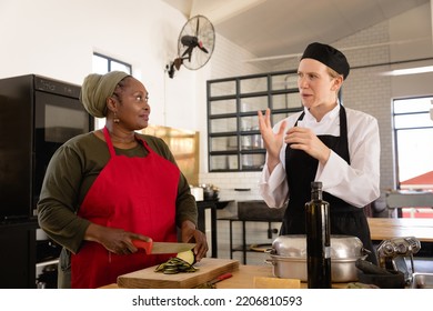 Front view of a Caucasian and an Senior African American woman at cookery class, the female chef in whites, talking while her female student chops a vegetable - Powered by Shutterstock